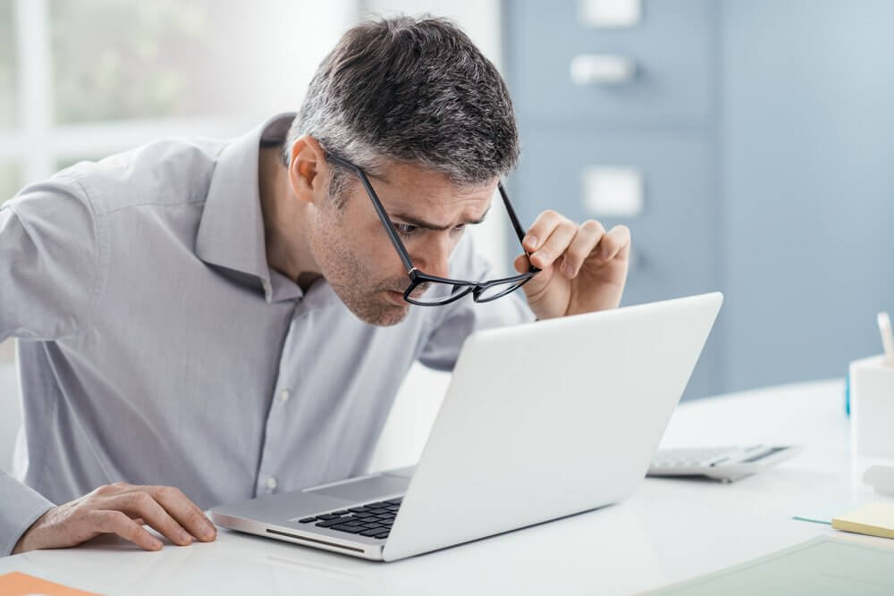 Man straining his eyes looking at a computer screen